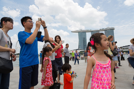 SINGAPORE - FEBRUARY 18, 2015: Tourists take pictures near the Merlion sculpture in the background of Singapore. In the background is the famous hotel and casino Marina Bay Sands.のeditorial素材