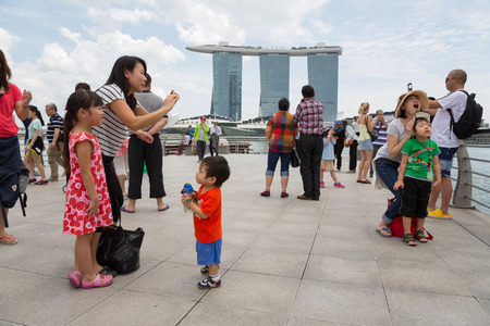 SINGAPORE - FEBRUARY 18, 2015: Tourists take pictures near the Merlion sculpture in the background of Singapore. In the background is the famous hotel and casino Marina Bay Sands.のeditorial素材