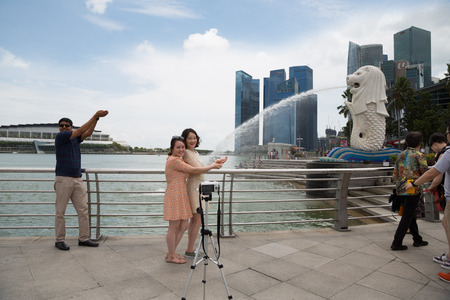 SINGAPORE - FEBRUARY 18, 2015: Tourists take pictures near the Merlion sculpture in the background of Singapore. Merlion is a imaginary creature with the head of a lion, seen as a symbol of Singaporeのeditorial素材