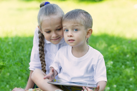 Brother and sister using tablet PC on the grass in summer park.の写真素材