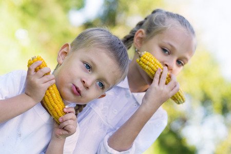 Sister and brother eating corn outdoorsの写真素材