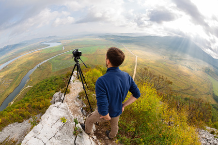 Photographer on top of the mountain takes a neighborhood on the camera. The sun's rays make their way through the clouds. Taken with a fisheye lens.の写真素材