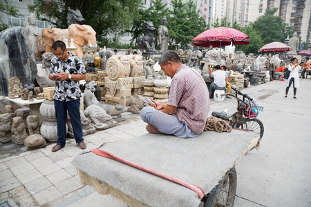 BEIJING - CIRCA JUNE, 2015: Rickshaw Man uses a smartphone while on the famous Panjiayuan Antique Market - one of the best antiques market in China. Area shopping area of 48 500 m2のeditorial素材