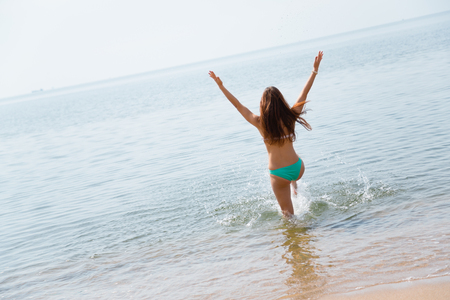 Happy young woman runs into the warm seaの写真素材