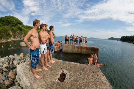 NAKHODKA, RUSSIA - JULY 29, 2015: Joyful boy and girl jumping into the sea from the old pier. Local children love to relax, sunbathe, swim and dive in the sea bay near the city of Nakhodka.のeditorial素材