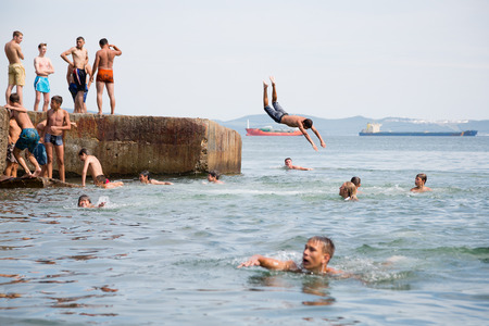 NAKHODKA, RUSSIA - CIRCA AUGUST, 2015: Joyful children jumping and diving into the sea from the old dock. Local children love to relax, sunbathe, swim and dive in the sea bay near the Nakhodka cityのeditorial素材