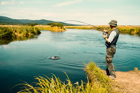 Middle aged man fishes caught pink salmon from the river. Far East Russia. Image retro vintage...