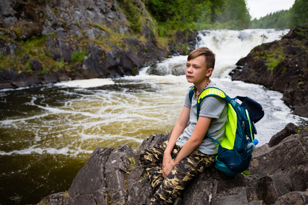 Teenager tourist with a backpack standing near the mountain waterfall.の写真素材