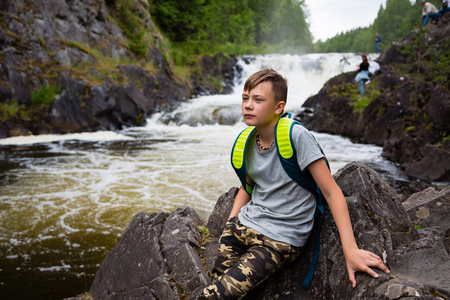 Portrait of a teenage boy standing near a waterfall in the summerの写真素材