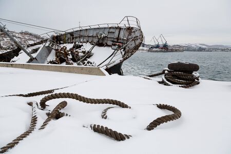 Mooring rope lies on a pier with a sunken ship in the winter. Environmental pollution.