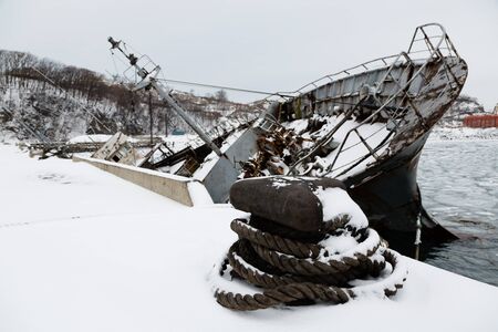 Old ship in disrepair sank at the pier in winter. Environmental pollution.