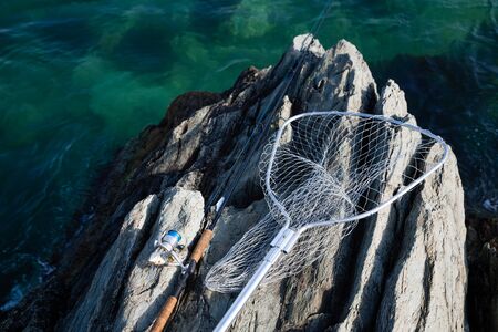 Spinning and landing net on a rocky shore by the seaの写真素材