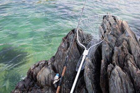 Spinning and landing net on a rocky shore by the seaの写真素材