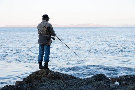 Fisherman on evening fishing on the rocks by the seaの写真素材