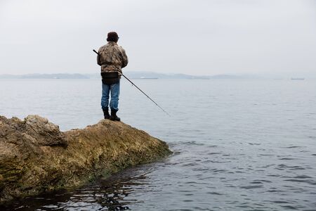 Fisherman on sea fishing on the rocks in the early morningの写真素材