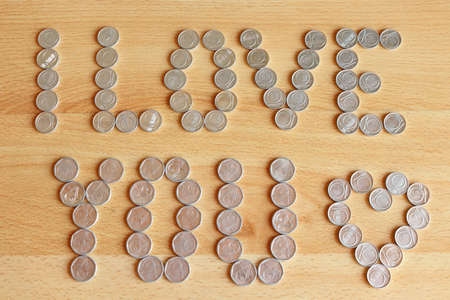 Inscription from coins on a wooden background - I love you - finished with a heart.の写真素材