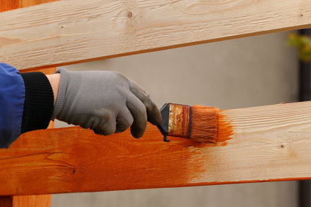 A hand holds a brush dipped in paint. Hand painting a wooden fence with brown glazing varnish.の写真素材