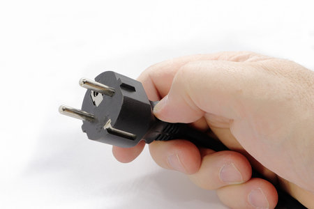 A hand holds an electric plug. Isolated on white background. Power supply cable.の写真素材