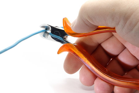 A hand holds a pair of pliers and cuts a blue wire. Isolated on white background.