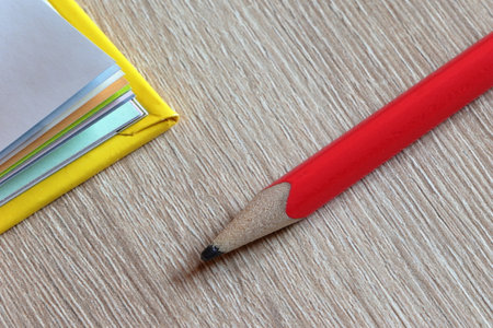 Close-up of a worn pencil on a wooden background. Corner of a yellow book with colorful pages.の写真素材