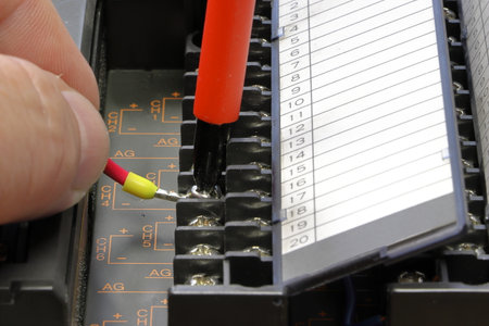 An electrical engineer connects a wire to a PLC terminal block. Fingers holding red wire. The screwdriver tightens the clamp.の写真素材