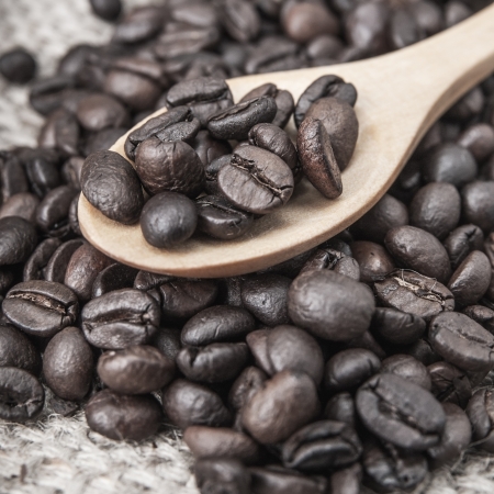 close up of coffee beans on wooden spoon with coffee beans on backgroundの写真素材