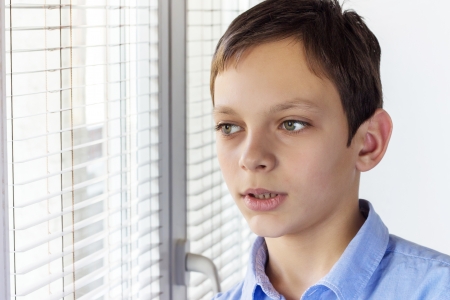 Handsome kid looking pensive through a windowの写真素材