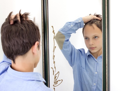 horizontal photograph of a young boy combing his hair while looking at himself in a mirrorの写真素材