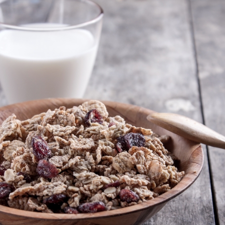 A bowl of cereal with cranberries and glass of milk on the tableの写真素材