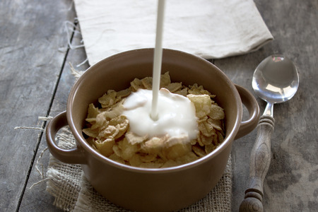 Bowl of cornflakes on wooden table. Natural light