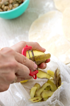 hands peeling potato with peeler, close up