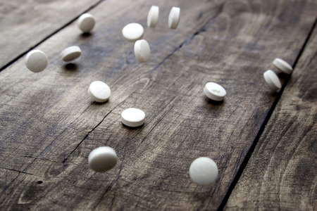 falling white pills over wooden background, close up