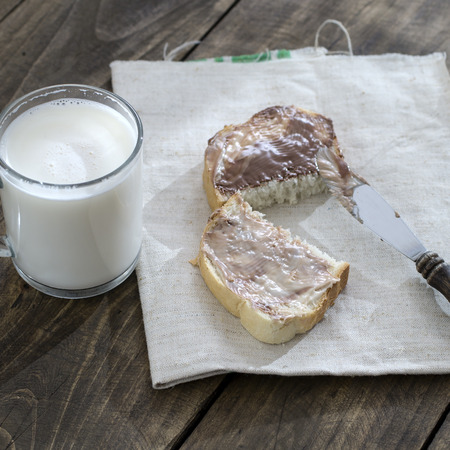 Slice of bread with chocolate cream and milk on tableの写真素材