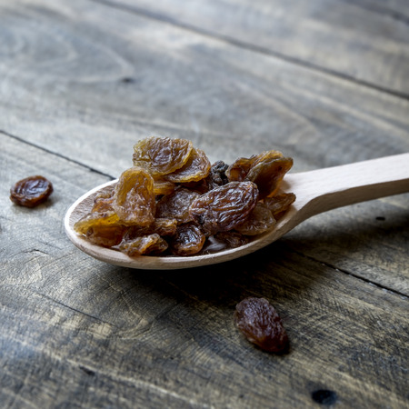 Tasty small black raisins on a wooden spoon, close upの写真素材