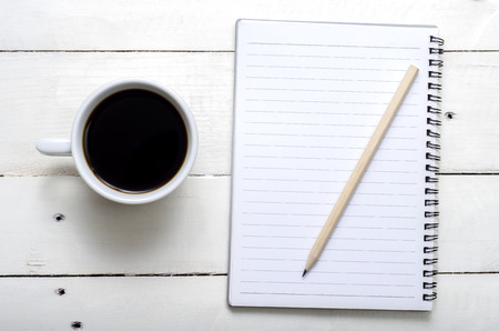 Hot coffee with notebook and pencil on white wooden tableの写真素材