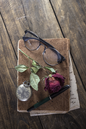 Still life with red rose on an old book placed with antique pocket watch on rustic wooden tableの写真素材