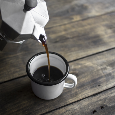 Pouring black coffee in the cup on the rustic wooden background