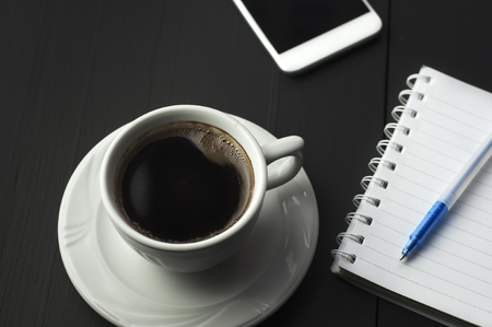 Smartphone with notebook and cup of coffee on dark wooden tableの写真素材