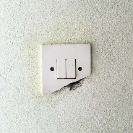 Old damage light switch on white wall, close upの写真素材