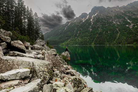 A girl is relaxing in the mountains, sitting on a rock near a beautiful lakeの写真素材