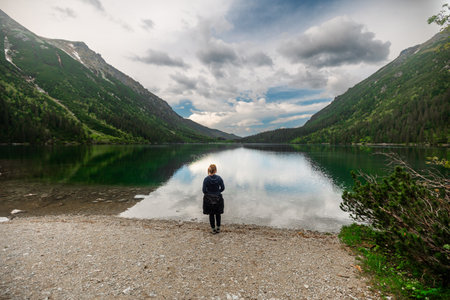 A girl is relaxing in the mountains, sitting on a rock near a beautiful lakeの写真素材