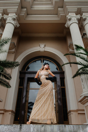 A beautiful young smiling woman in a vintage long gold dress in the style of gangster America of the...