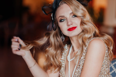 A beautiful young smiling woman in a vintage gold dress in the style of gangster America 1920-1950 with a decoration of black feathers on her head in a vintage interiorの写真素材