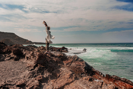 Full female body in white clothes on a rocky beach by the ocean in summer in the Canary Islandsの写真素材