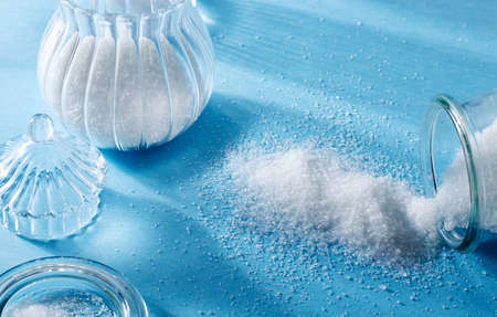 Closeup of scattered sugar and sugar in a glass bottle, on blue background