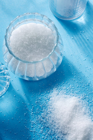 Closeup of scattered sugar and sugar in a glass bottle, on blue background