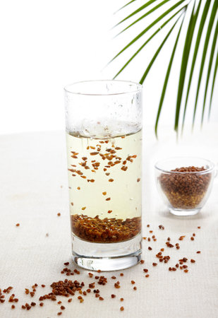 Flax seeds in a glass of water and a palm leaf on a white backgroundの写真素材
