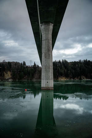 Bridge over turquoise water in winter with overcast sky and forestの写真素材