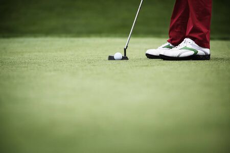 Feet of female golf player putting at green, with plenty of copy-space.の写真素材