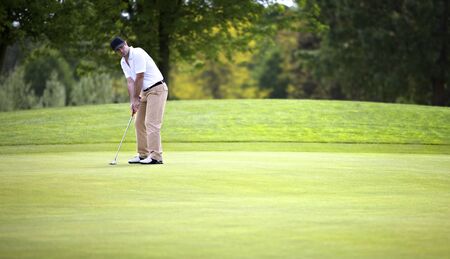 Golf player concentrating for putting golf ball on green.